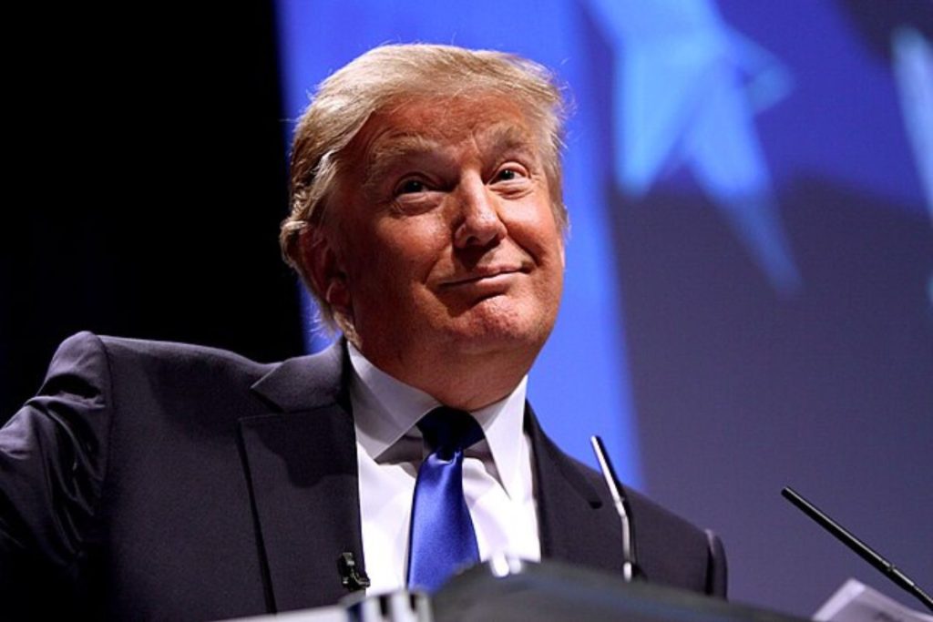 Donald Trump comenta ataque do Irã à base dos EUA no Catar durante discurso, com expressão confiante e fundo azul com estrelas ao fundo