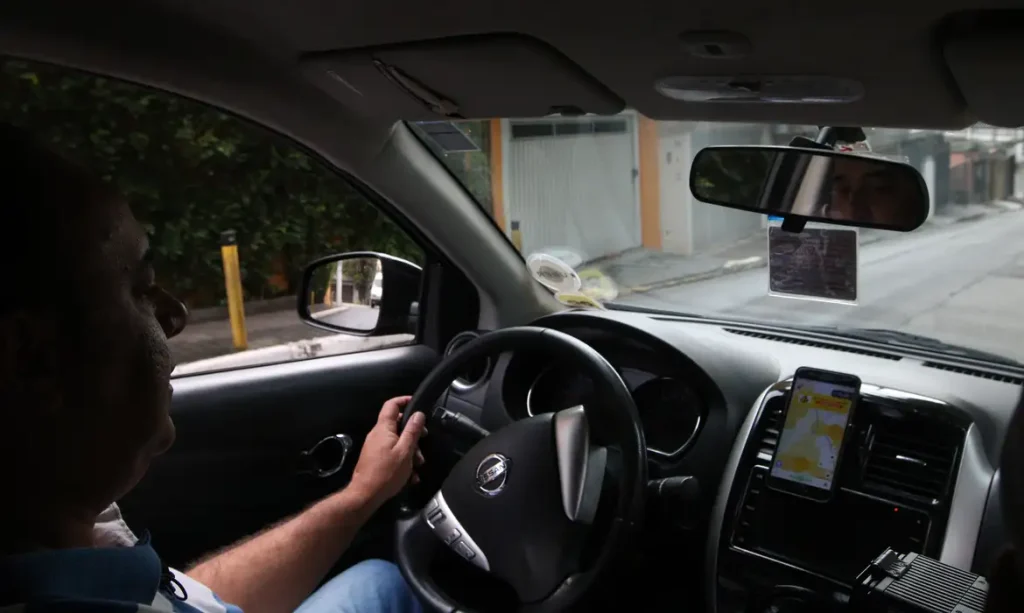 Motorista de transporte por aplicativo utilizando celular no painel do carro para visualizar informações de rota e ganhos.