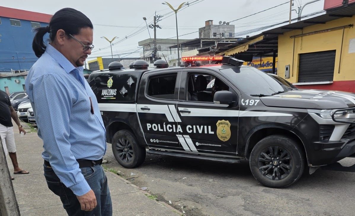 Policial militar atende homem ferido sentado na frente da delegacia do 9º DIP em Manaus