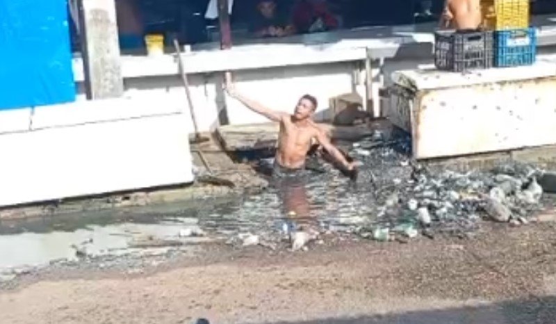 Homem dentro de bueiro realizando limpeza manual sem equipamentos de segurança na Feira da Liberdade em Manacapuru