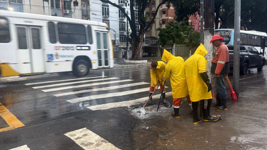 Equipes da prefeitura de manaus realizam limpeza e desobstrução de bueiros no centro da cidade durante dia de chuva forte.