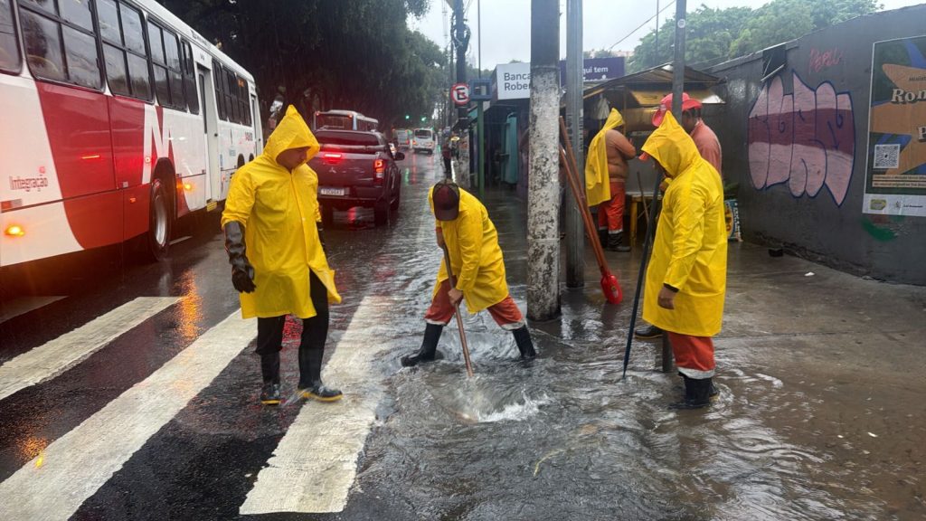 Equipes da prefeitura de manaus realizam limpeza e desobstrução de bueiros no centro da cidade durante dia de chuva forte.