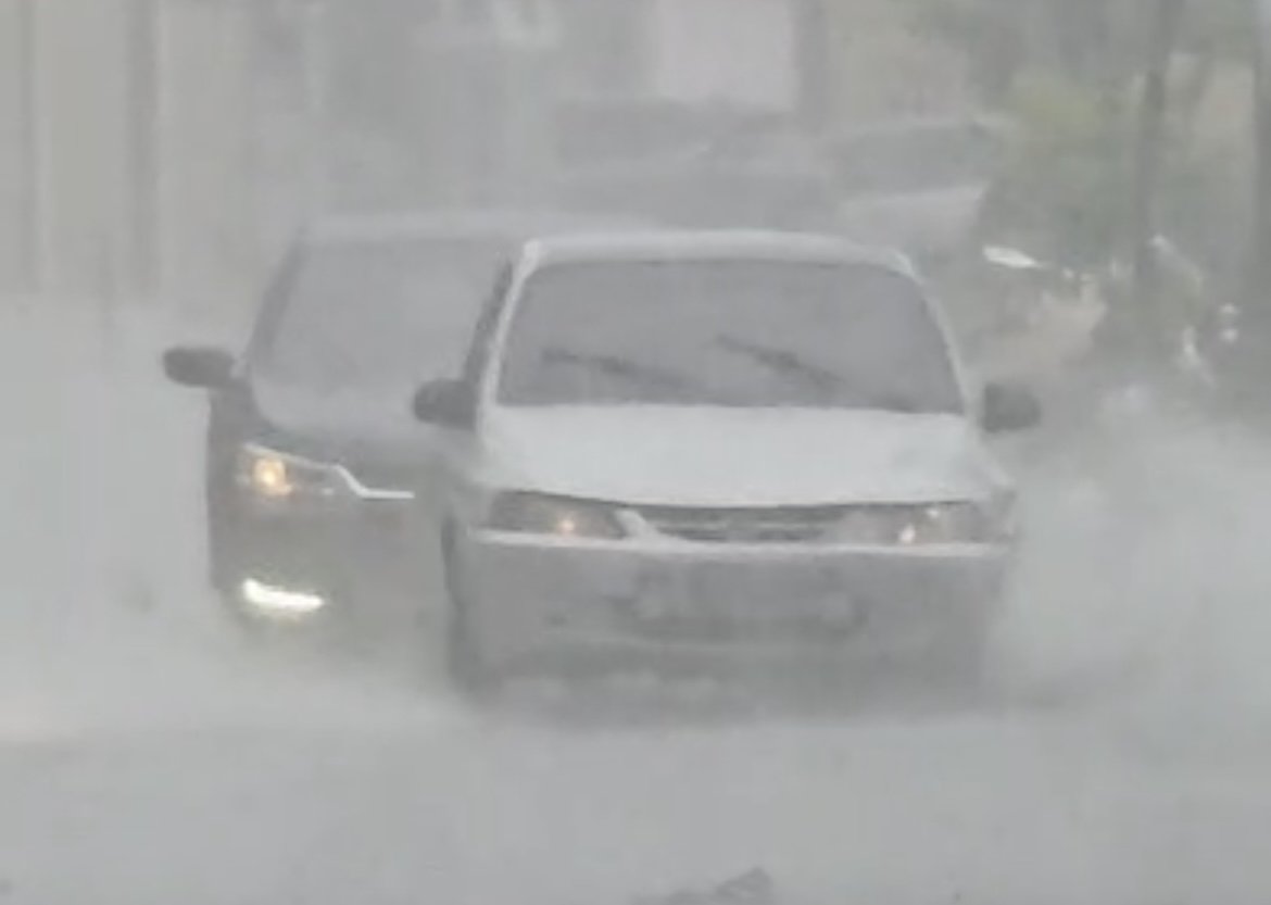 Avenida alagada em Manaus com carros enfrentando acúmulo de água durante temporal.