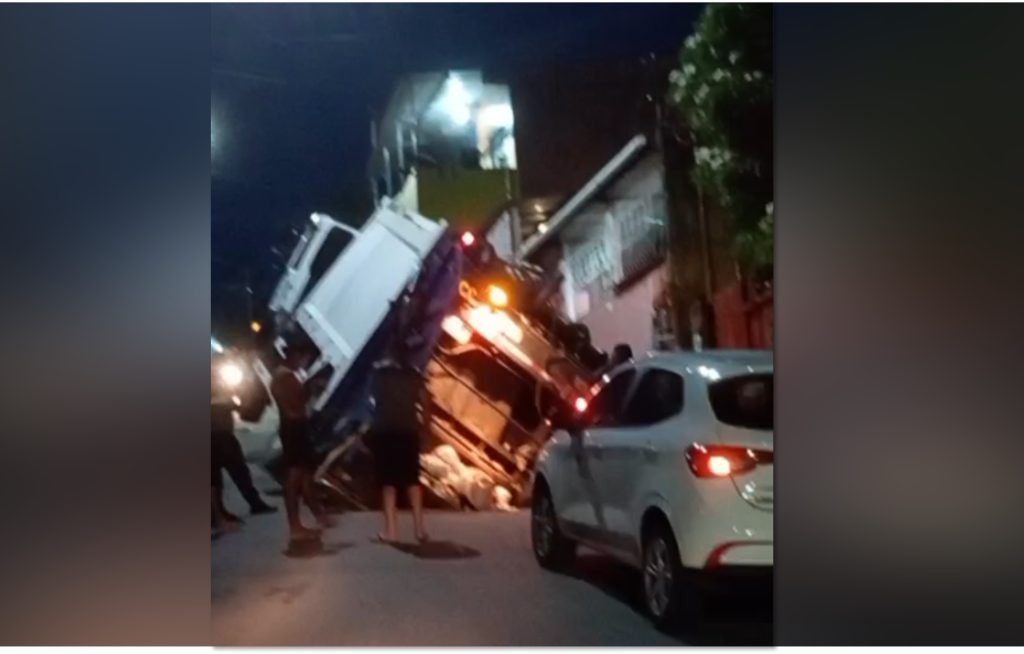 Caminhão de coleta de lixo preso em uma cratera aberta no asfalto na rua Raimundo Maia em Manaus.
