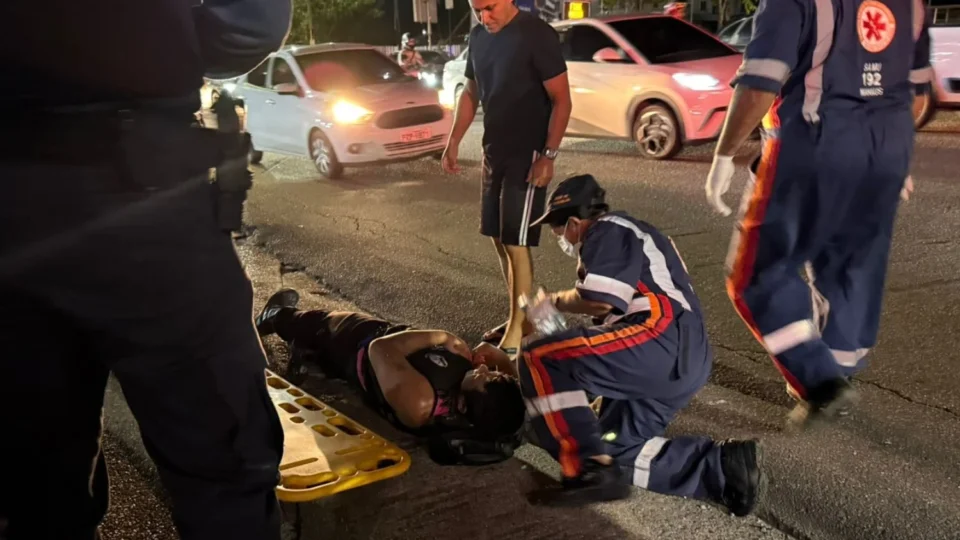 Motociclista caído no asfalto da Avenida Coronel Teixeira em Manaus após colisão com carro modelo Gol branco.