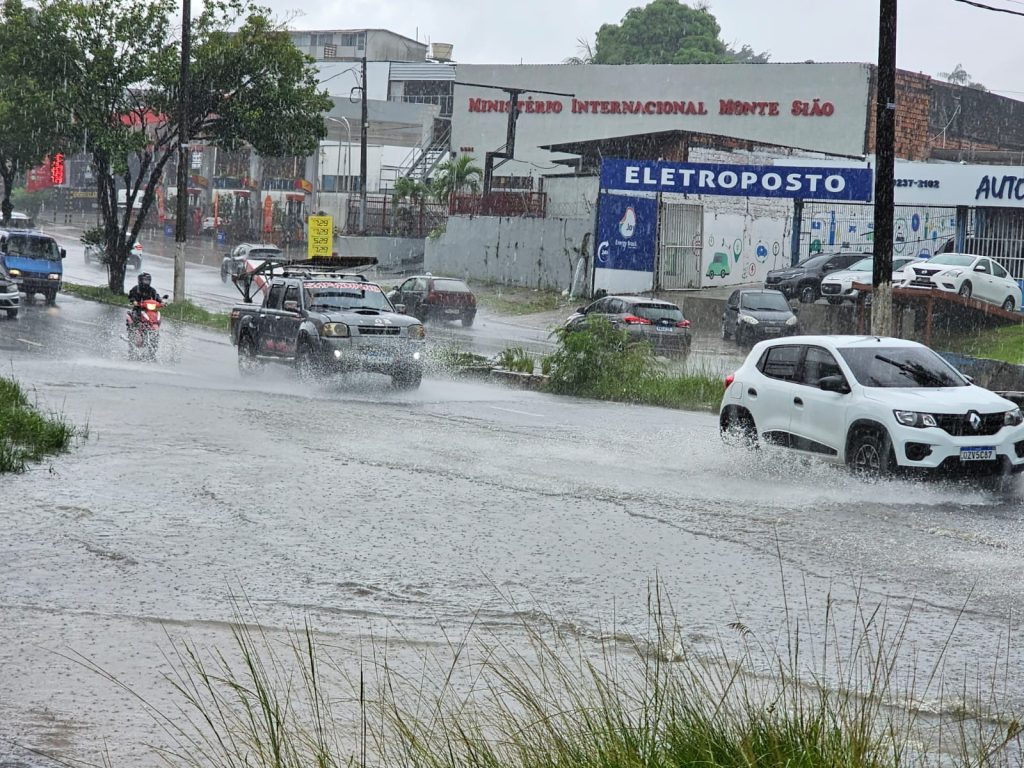 Vista de rua em Manaus com pontos de alagamento e veículos trafegando sob chuva forte na Alameda Cosme Ferreira.