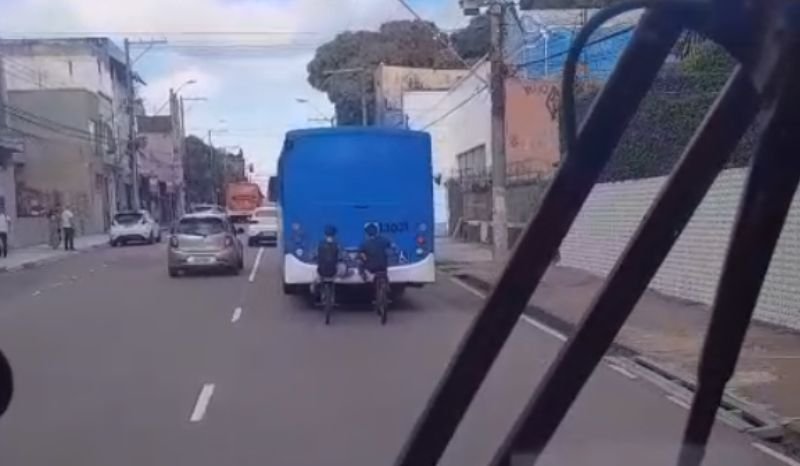 Jovens segurando na traseira de um ônibus em movimento no centro de Manaus